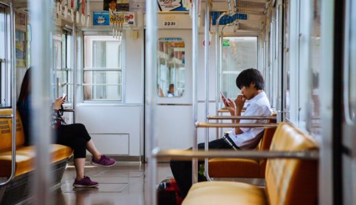 電車でスマートフォンをいじっている男子学生